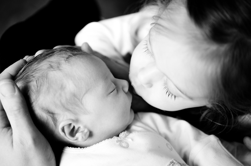 Professional colour photograph of big sister kissing new baby