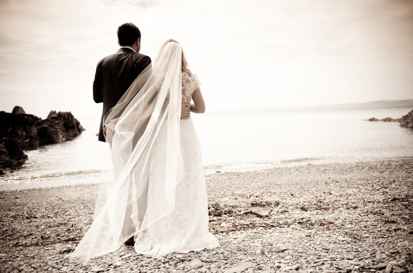 Professional colour photograph of bride and groom cuddling on a beach